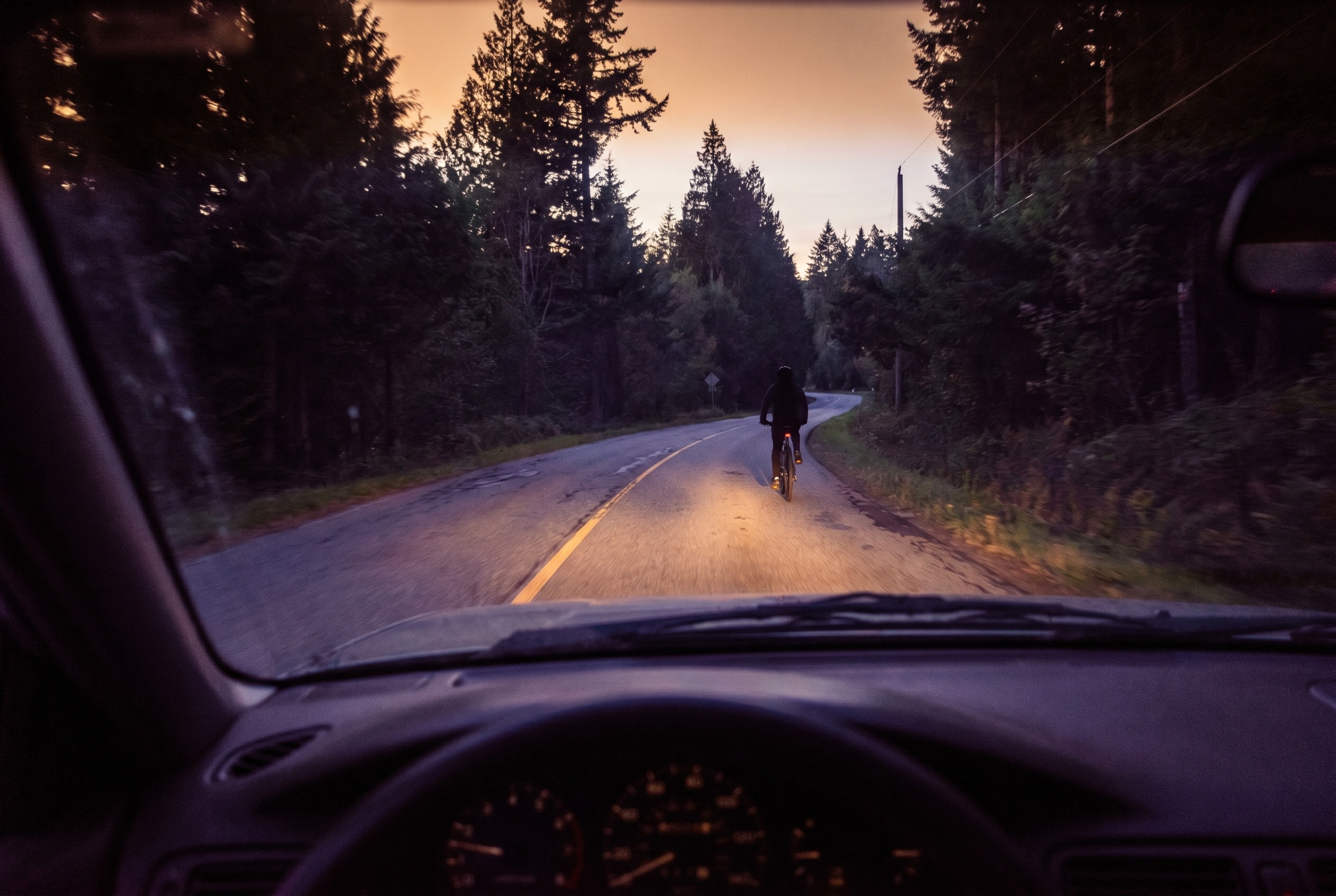 You are driving at dusk and notice a cyclist without lights ahead. What should you do?