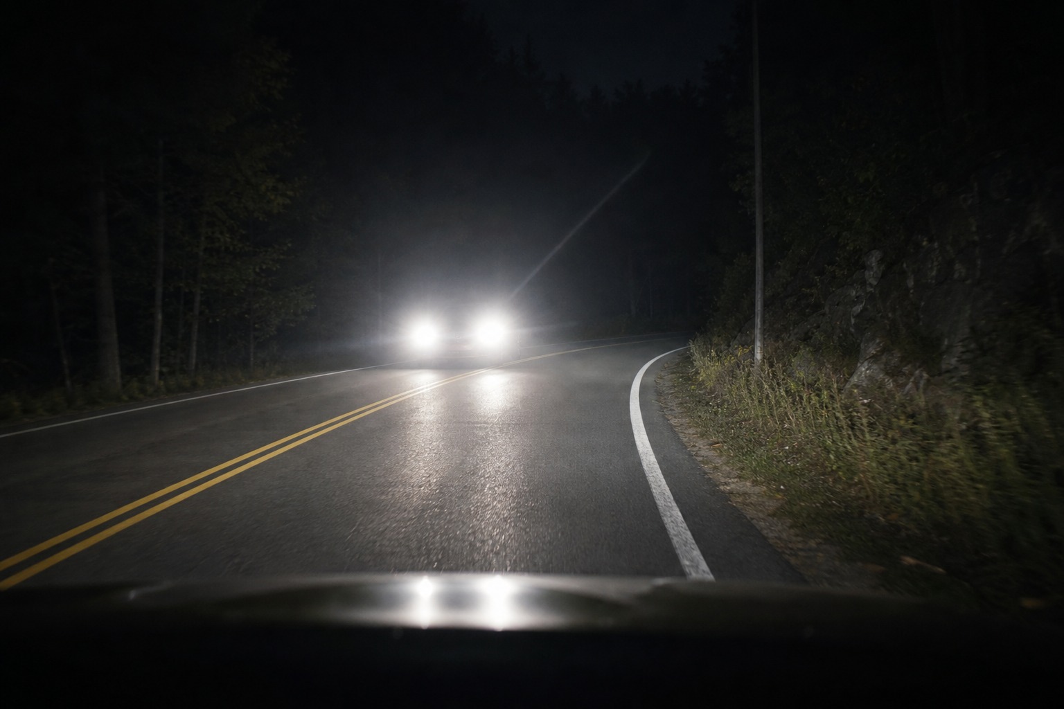 In the image, bright oncoming headlights are causing glare at night. What should you do?